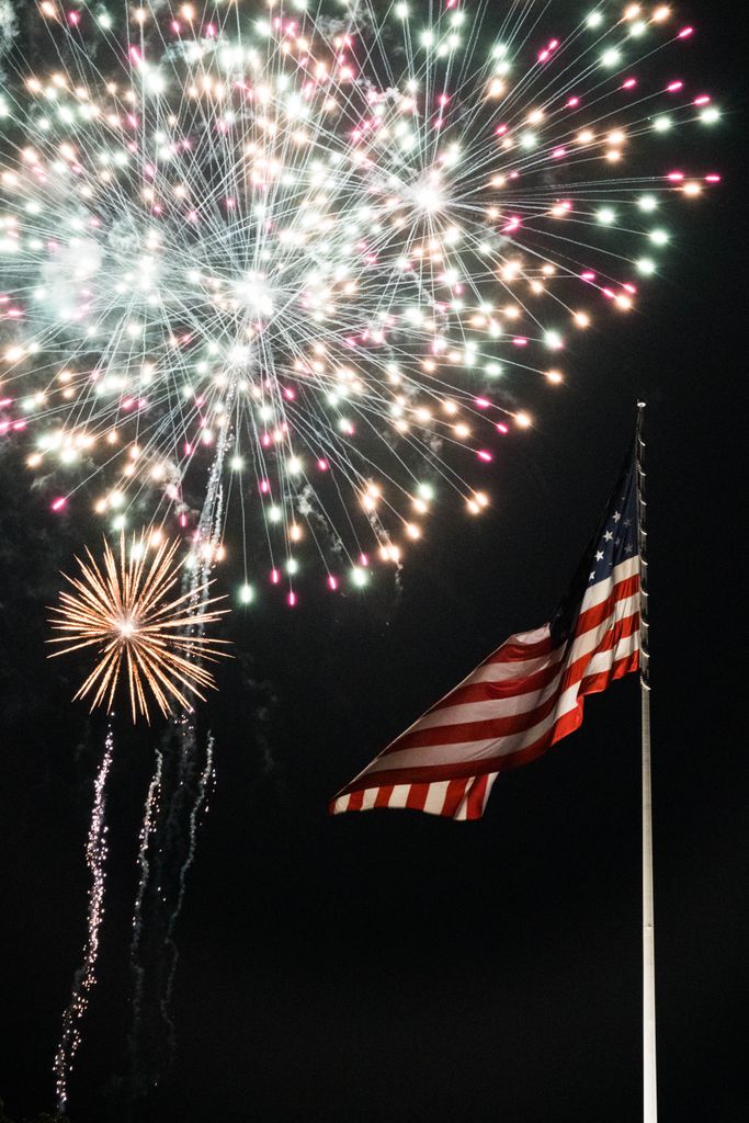 Colorful fireworks illuminate the night sky above the American flag in New York City.